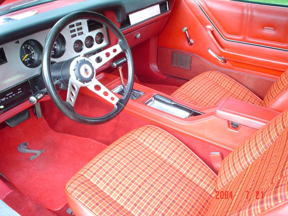 Red interior of a 1978 Ford Mustang II with plaid seats and a four-spoke steering wheel