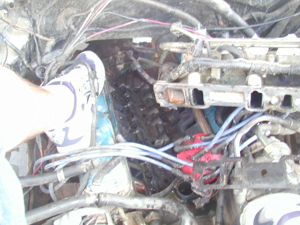 Engine bay with a foot on the engine block, showing spark plug wires and intake manifold