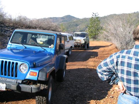 1989 Ford Bronco - Two off-road vehicles, a Jeep and a Ford Bronco, travel on a dusty trail.