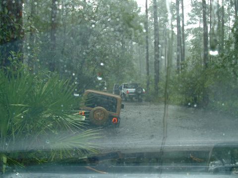 1995 Ford Bronco - Two SUVs navigate a muddy forest road under heavy rain.