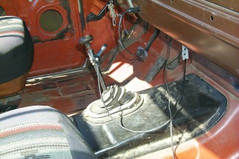 1978 Ford Bronco - The interior of a vehicle displays a manual transmission shifter and a hand throttle lever, with visible wear on the floor.