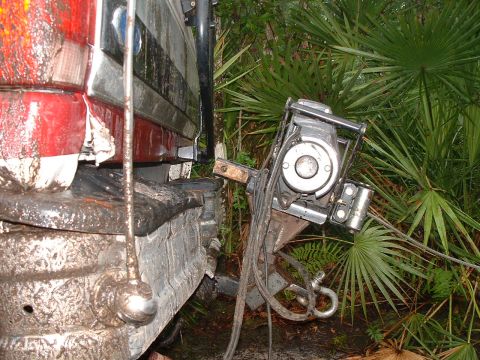 1995 Ford Bronco - The rear of a 1995 Ford Bronco is shown with a winch attached to its bumper, surrounded by foliage.