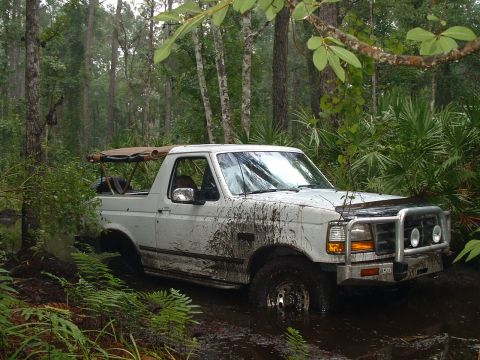 1995 Ford Bronco - A white Ford Bronco navigates a muddy trail through a dense forest.