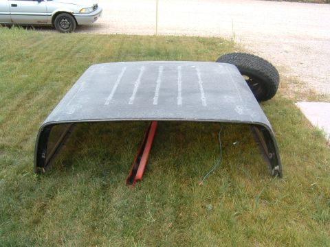 1987 Ford Bronco - A detached vehicle roof is on the grass next to a spare tire. Another car is visible in the background.
