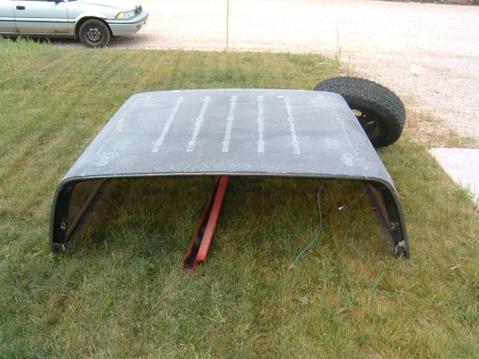 removed vehicle roof sitting on grass, spare tire nearby