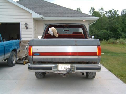 1987 Ford Bronco - Rear view of a 1987 Ford Bronco parked in a driveway next to a blue pickup truck.