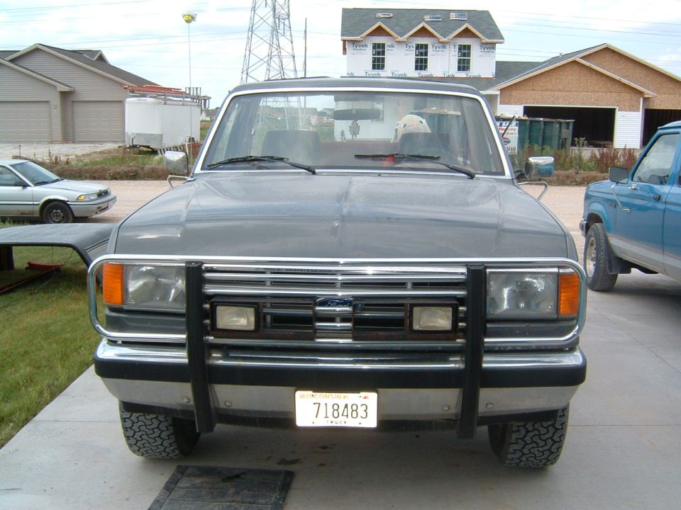1987 Ford Bronco front end with bull bar and license plate 718483. Blue Ford Bronco visible to the right