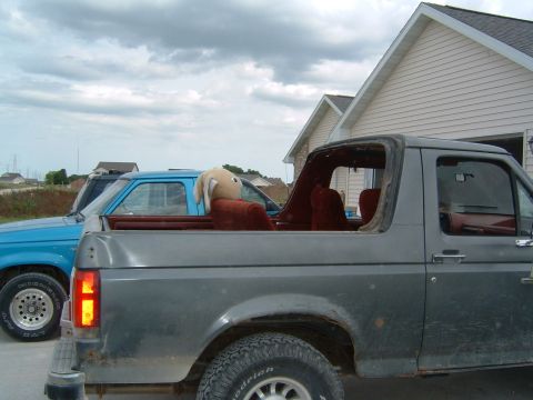 1987 Ford Bronco - A gray 1987 Ford Bronco is parked next to a blue truck under a cloudy sky.