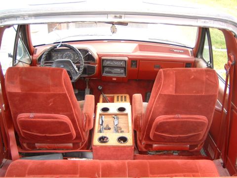 1987 Ford Bronco - The interior of a 1987 Ford Bronco, red velour upholstery and a wooden center console with cup holders.