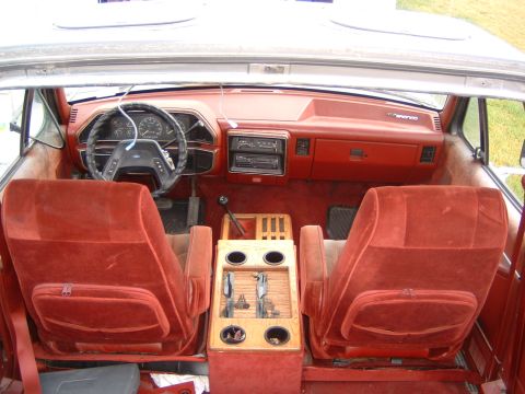 1987 Ford Bronco - The interior of a 1987 Ford Bronco shows red velour seats and a woodgrain center console.