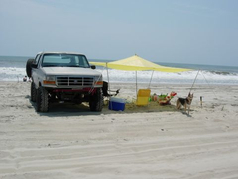 1995 Ford Bronco - A lifted 1995 Ford Bronco is parked on the beach near the ocean waves, set up for a day of relaxation.