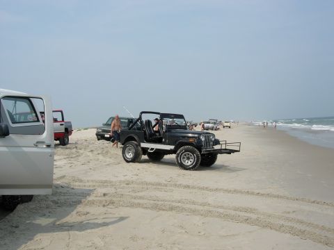 1995 Ford Bronco - Several vehicles are parked on the sand near the ocean on a sunny day.