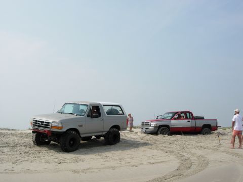 1995 Ford Bronco - Two trucks are parked on a sandy beach with the ocean in the background.