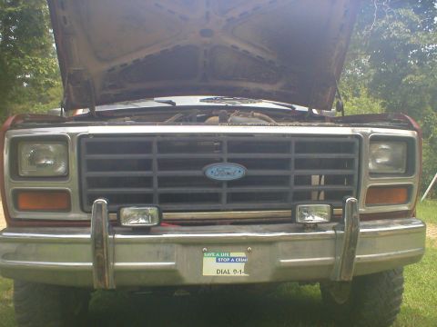 1986 Ford Bronco - Front view of a 1980s Ford Bronco grille, showing the headlights and bumper. Hood is open.