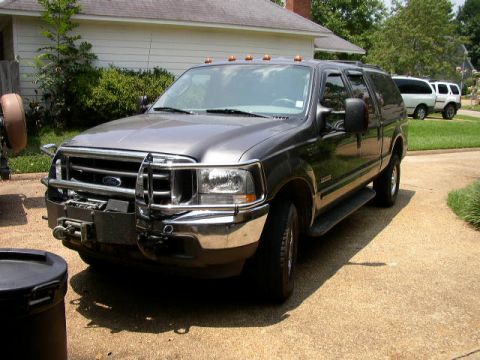 1995 Ford Bronco - This gray SUV, likely a Ford Excursion from around 2003, is parked in a driveway with another white SUV visible in the background.