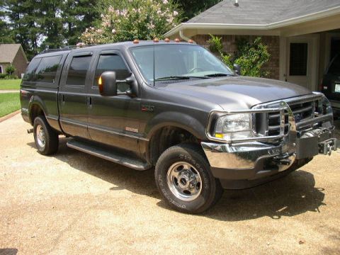 1995 Ford Bronco - This Ford Super Duty truck features a chrome grille guard and a camper shell, parked in a suburban driveway.