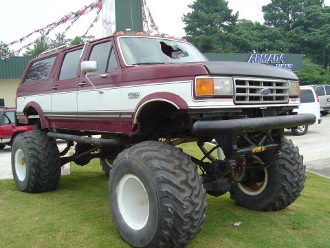 1986 Ford Bronco - This heavily modified Ford Bronco sits on massive tires, a two-tone paint job and a damaged windshield.