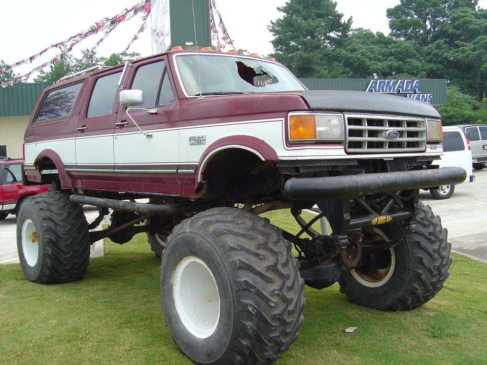 Maroon and white lifted Ford Bronco with large tires, cracked windshield, and aftermarket bumper