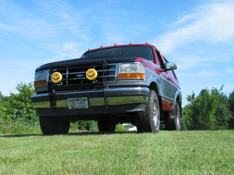 1995 Ford Bronco - A red and silver Ford Bronco is parked on a grassy lawn under a blue sky.