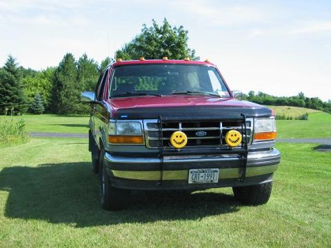 1995 Ford Bronco - A red Ford truck from the early 1990s is parked on a grassy lawn under a clear blue sky.