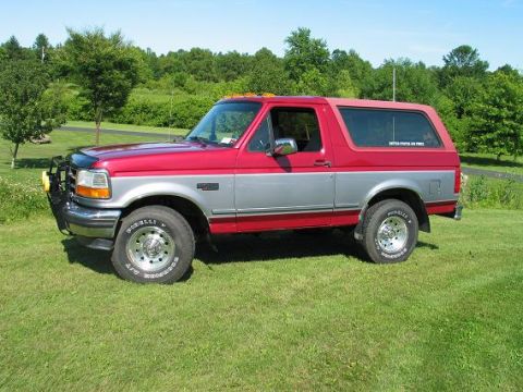1995 Ford Bronco - This two-tone red and silver 1995 Ford Bronco is parked on a grassy lawn with trees in the background.