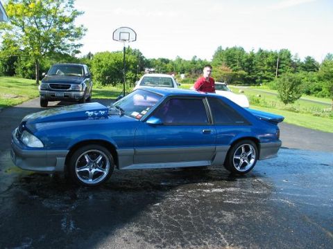 1990 Ford Mustang - Blue 1990 Ford Mustang with aftermarket hood and gray lower trim is parked on wet asphalt.