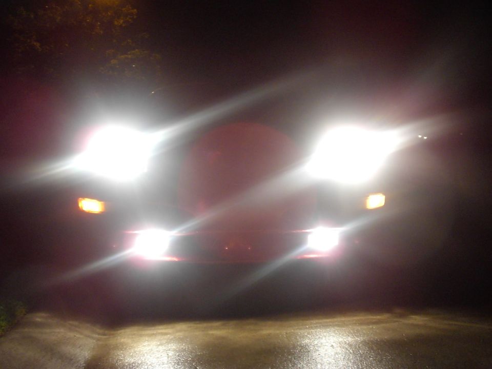 Blurry nighttime shot of a car's headlights and fog lights glaring in the dark