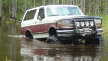 1993 Ford Bronco - 1993 Ford Bronco navigating a water-filled wooded area.