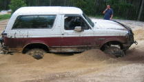 1993 Ford Bronco - A Ford Bronco is stuck in a muddy area, with a person standing in the background.