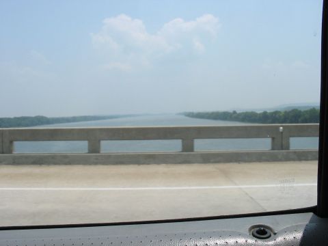 1988 Ford Bronco - View from a vehicle traveling over a bridge, looking out at a wide river and the distant tree-lined shore.