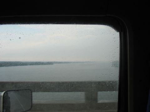 1988 Ford Bronco - Raindrops on the window obscure the view of a calm body of water and the distant shore.