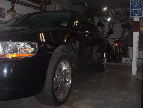 1989 Ford Bronco - A black sedan is parked inside a garage with bicycles and other vehicles in the background.