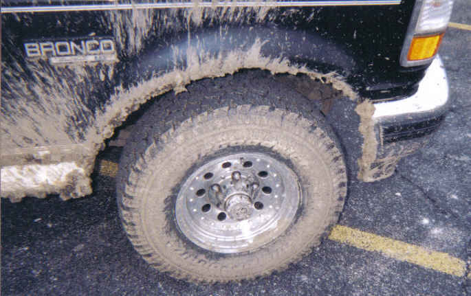 Mud-caked tire and wheel on a black Bronco with BRONCO lettering on body