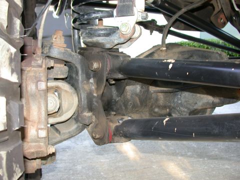 1996 Ford Bronco - Detailed underside shot of a solid front axle on a lifted 4x4, showing the cast knuckle and rusty disc brake caliper at left, the coil spri…