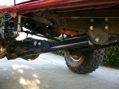 1996 Ford Bronco - An underbody view of a lifted red 4x4 on a concrete driveway, showing the front suspension: black coil springs, a shock with a black boot,…