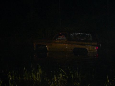 1989 Ford Bronco - A yellow pickup truck is submerged in water at night, with only its upper body visible above the surface.
