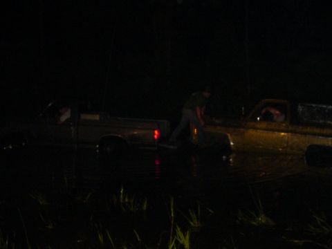 1989 Ford Bronco - Two trucks are stuck in the water at night, with a person visible near one of them.