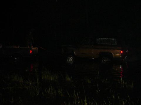 1989 Ford Bronco - A person stands between two vehicles in the water at night, with one vehicle being towed by the other.
