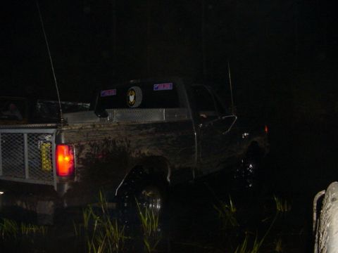 1989 Ford Bronco - A muddy Ford truck is partially submerged in water at night, viewed from the rear.