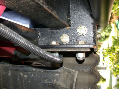 1996 Ford Bronco - Close-up under a truck showing a black-painted boxed steel bracket bolted to the frame rail with large yellow-zinc hex bolts and a stack of…