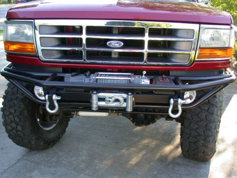 1996 Ford Bronco - Front view of a red 1990s Ford Bronco with a black tubular winch bumper, mounted winch with hook, and two silver D-ring shackles. The truck…
