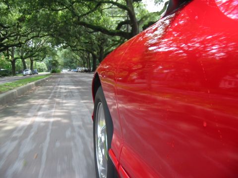 1997 Ford Probe - A red 1997 Ford Probe is captured from the side as it drives down a street lined with trees.