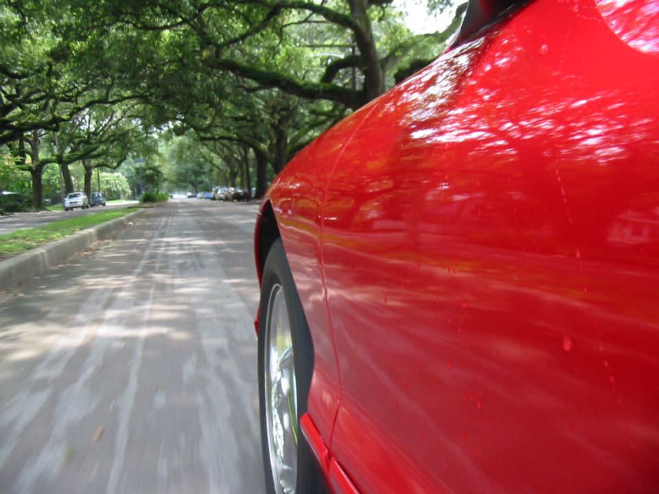 Red car front fender and alloy wheel in motion on a tree-lined street