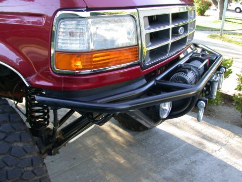 1996 Ford Bronco - Close-up 3/4 front view of a dark red 1990s Ford Bronco/F-series with a chrome grille and amber/clear headlight, fitted with a heavy black…