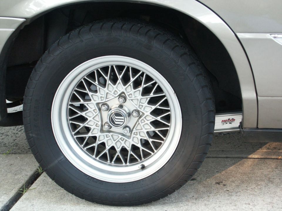 Lacy multi-spoke alloy wheel and tire on a tan sedan, close-up