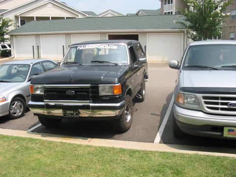 1988 Ford Bronco - Two trucks parked in a lot, one is a black Ford Bronco and the other is a silver Ford F-150.