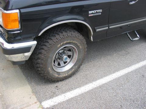 1988 Ford Bronco - Close-up of the front wheel and fender of a black Ford Bronco, showing the 'Bronco' badge.
