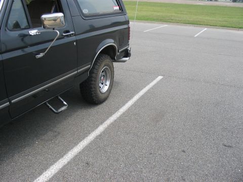1988 Ford Bronco - A dark SUV is parked in a lot, showing its side profile and wheel.