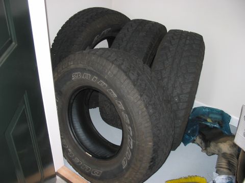 1988 Ford Bronco - Four Bridgestone Dueler A/T tires are stacked against a wall.