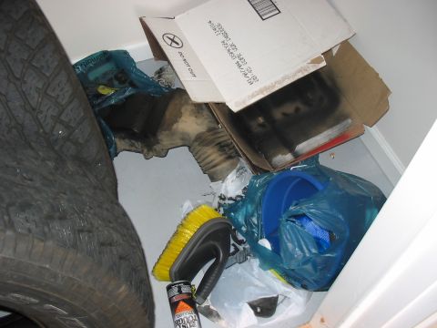 1988 Ford Bronco - A collection of automotive parts and cleaning supplies are stored together, including a tire, a brush, and various components in boxes and…